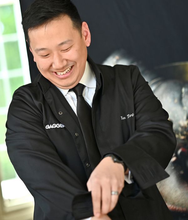 Chef Yuan Tang smiling, adjusting his jacket sleeves. 