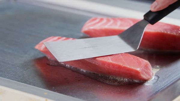 A metal spatulas being used while cooking salmon fillets on the Gaggenau Vario Teppan Yaki