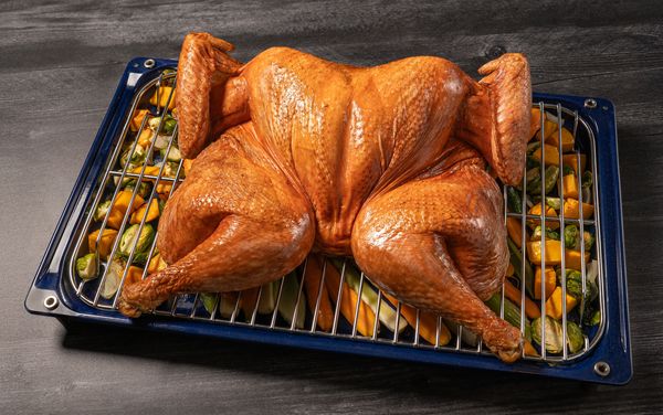 Spatchcocked turkey on a wire tray with a selection of diced vegetables on the oven tray underneath the turkey