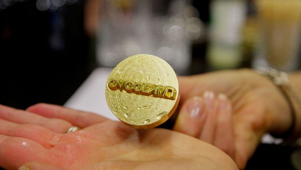 Hands holding a round, golden metal stamp with "Gaggenau" embossed on its surface.
