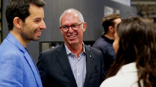 A smiling man with glasses chats with guests at an event.