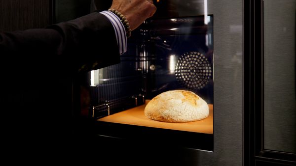 A hand opens an oven, revealing a freshly baked loaf of bread.