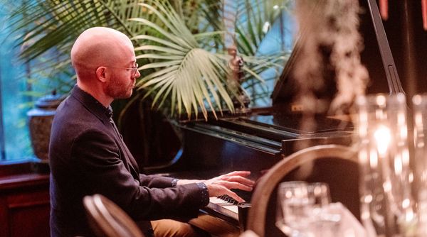In the warm, sultry lighting of the Grand Salon, a pianist plays at a grand piano for guests.