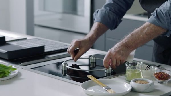 Kitchen scene with a man placing a wok ring onto a Gaggenau vario induction cooktop  