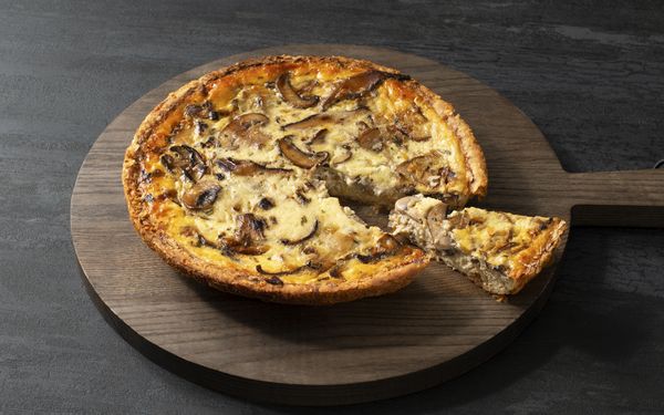 A mushroom and leek quiche displayed on a chopping board with a slice neatly cut out