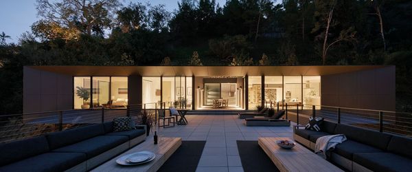 The top floor of the LR2 House lights up the night, set against the forest backdrop.