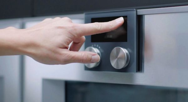 A hand interacting with the TFT display on a Gaggenau oven