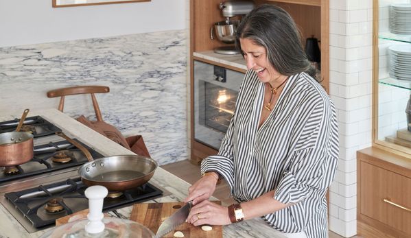 A woman chopping vegetables and smiling next to her Gaggenau cooktop. 