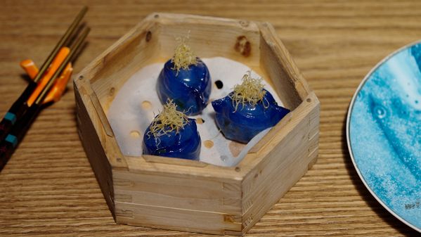 A blue omni-spinach dumpling served in a wooden box 