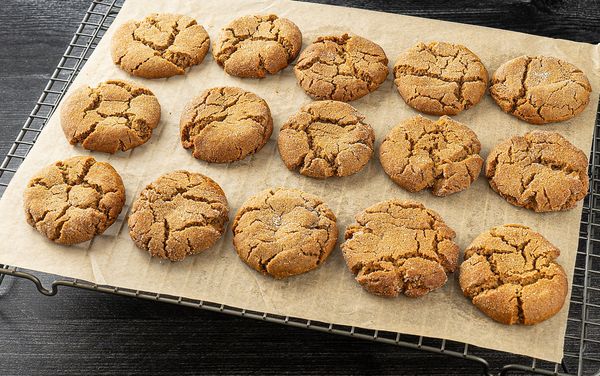 Ginger molasses cookies laid out across parchment paper upon a cooling rack.