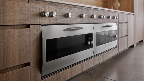 Two Gaggenau EB 333 ovens displayed in the Houston Flagship showroom, surrounded by textured plaster and natural wood 