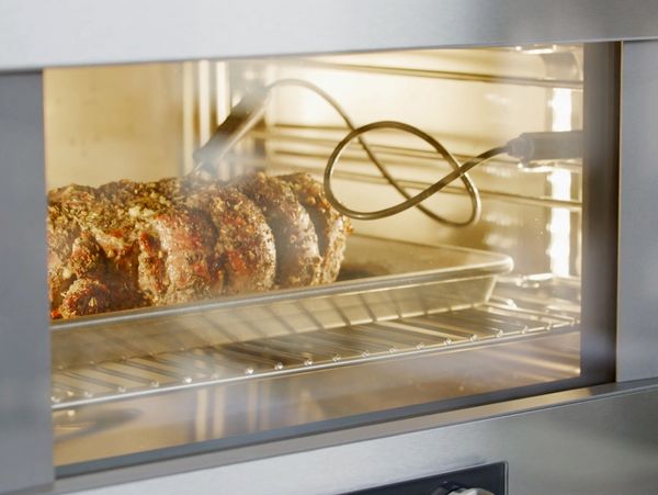 Close-up view of a Gaggenau combi steam oven cooking a piece of meat with a core temperature probe inserted 