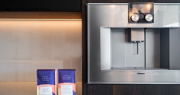 A close-up of a Gaggenau coffee machine, next to bags of authentic Kona coffee. 