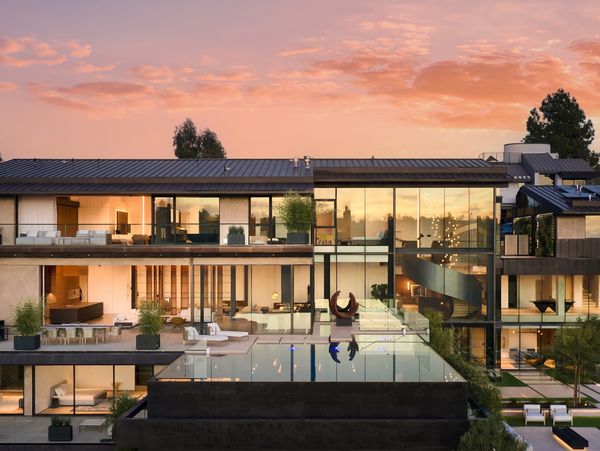 Exterior of César Giraldo's stunning Bel Air project at sunset, with the home's glass exterior mirrored in the infinity pool below. 