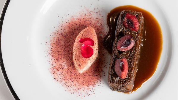 The final dish of the evening, named Campfire Under the Chestnut Tree, featuring an ember fired chestnut cake with whiskey butterscotch, rose petal whipped cream, cherries, and dried rose petal powder.