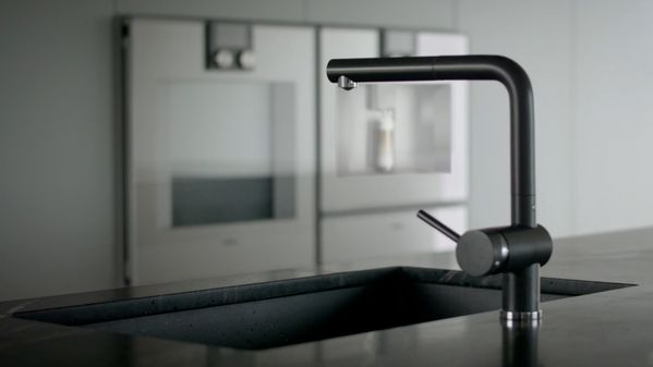 A tap and sink in  the foreground with Gaggenau appliaces behind