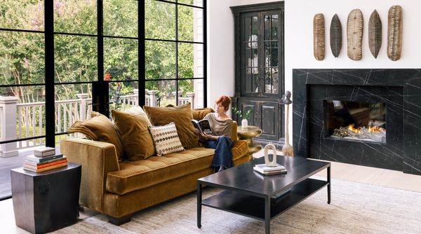 Jan Mengenhauser seated in front of the ceiling-height windows of her living room, next to a warm fireplace. 