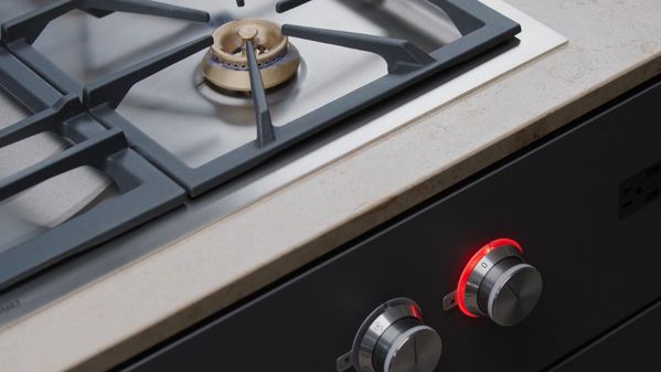 The flame from one of the standard output burners of a Gaggenau 5 Burner Vario Gas Cooktop with its associated control knob illuminated