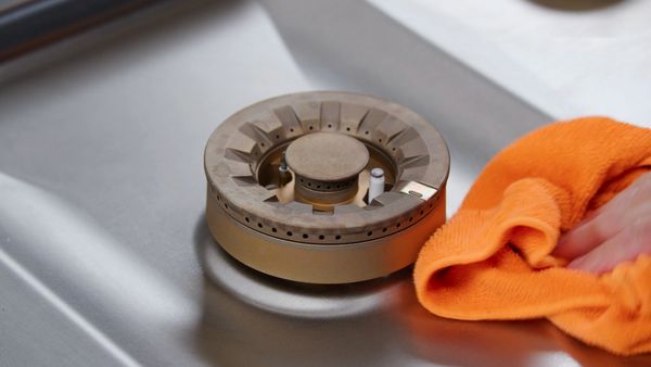 A hand cleans the stainless steel of the Gaggenau 5 Burner Vario Gas Cooktop