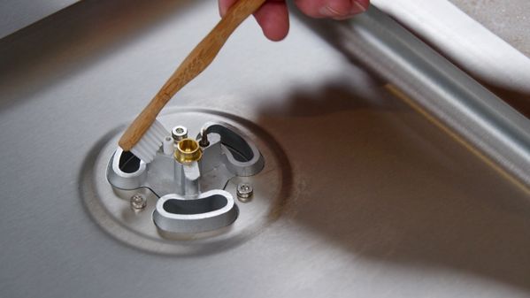 Using a small soft brush, a hand carefully cleans the ignition plug of the Gaggenau 5 Burner Vario Gas Cooktop