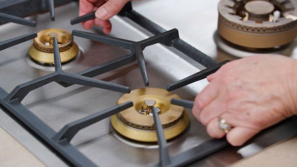 A pair of hand carefully removes the cast iron grate of the Gaggenau 5 Burner Vario Gas Cooktop to avoid scratching the stainless steel