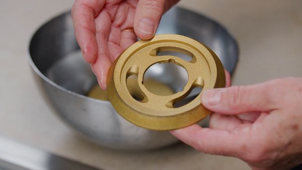 A pair of hands cleaning the brass burner of the Gaggenau 5 Burner Vario Gas Cooktop