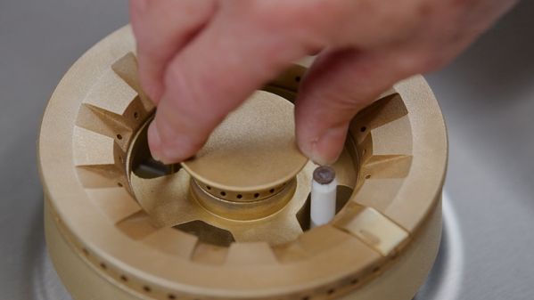 A hand carefully locking the brass burner of the Gaggenau 5 Burner Vario Gas Cooktop in place after cleaning