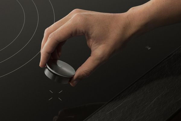 A hand places the magnetic twistpad onto the Gaggenau flex induction cooktop.