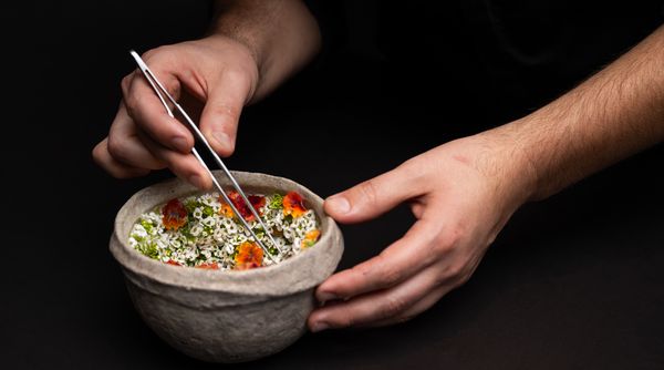 A chef carefully places flowers on one of Vespertine's elegant dishes.