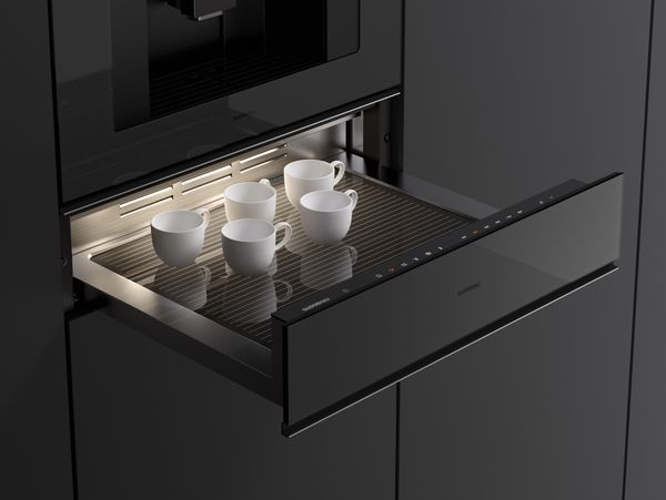 Close-up of an open Gaggenau Minimalistic series culinary warming drawer containing small coffee cups