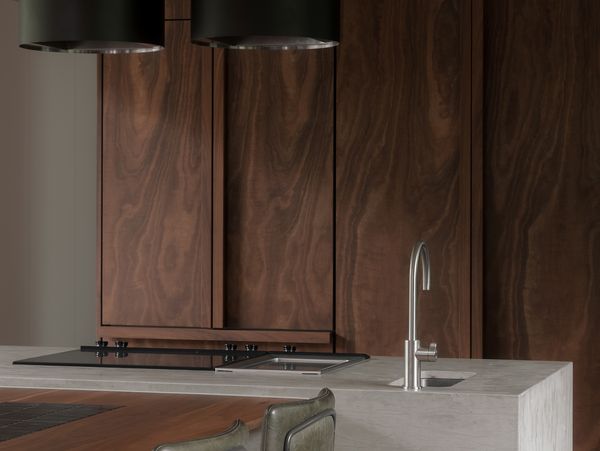 Concrete kitchen island with Gaggenau Vario 400 series cooktops and two black ceiling-mounted extractor hoods.