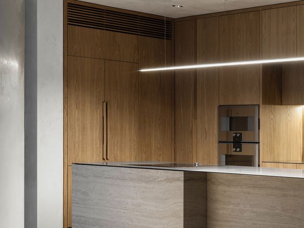 A modern kitchen with a stone island, wood cabinetry, and an integrated Gaggenau 200 series oven