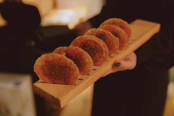 A hand holding a wooden platter of small, round fried pastries.