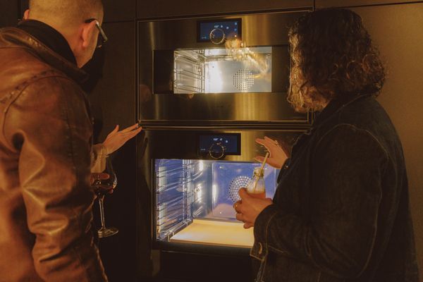 Two individuals examining the interior of Gaggenau ovens, illuminated by soft lighting for an inviting atmosphere