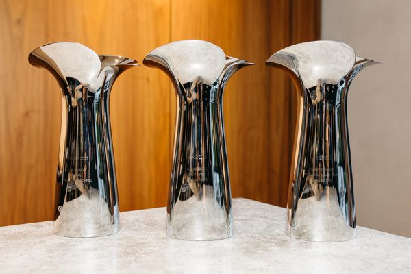 Three polished silver, petal-shaped trophies displayed on a light stone surface.