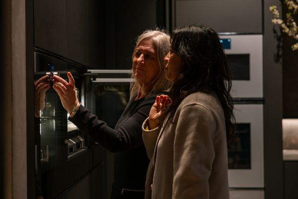 Two women inspecting the controls of a built-in Gaggenau oven in a kitchen.