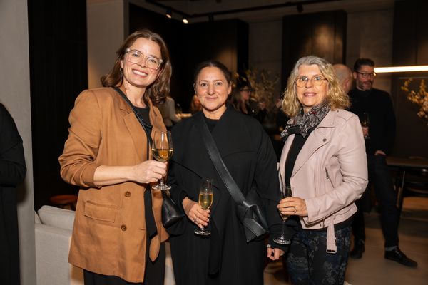 Three women smile together, holding glasses of wine during a sophisticated evening event.