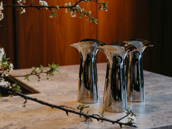 Three polished silver vases on a stone surface with white cherry blossom branches.