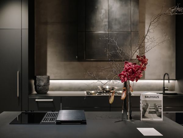 Dark, modern Gaggenau kitchen with integrated cooktop, a striking floral arrangement, and a Bauhaus magazine on the island.